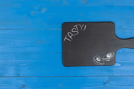 Black stone tray with Tasty sign above blue wooden background with copy space.の写真素材