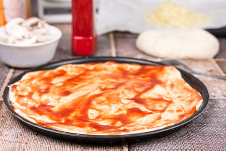 Raw pizza dough coated with tomato ketchupの写真素材