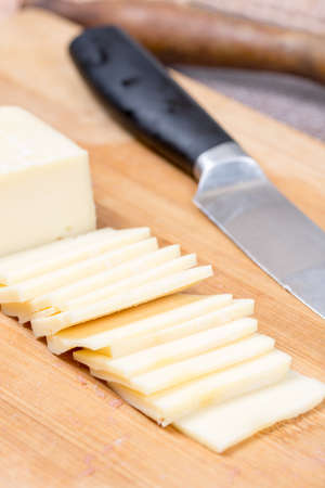 Sliced yellow cheese on the kitchen wooden board with knife