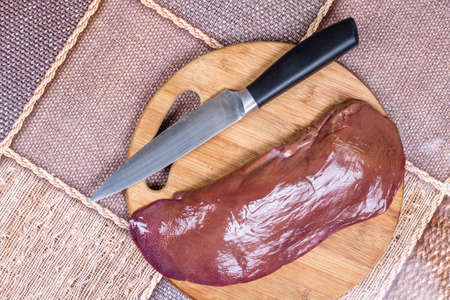 Fresh raw pork liver on wooden kitchen board with knife