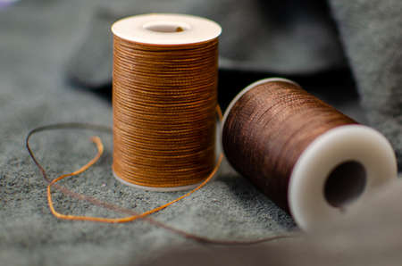 two spools of brown thread on a black inverted leather background