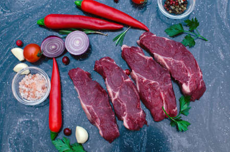 Four raw, fresh steaks with rosemary, garlic and spices on a marble table.
