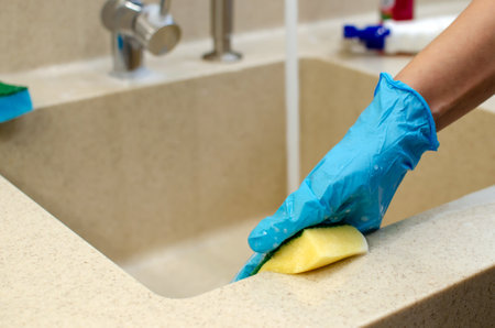 Woman doing housework in the kitchen at home, cleaning the sink and faucet with a yellow sponge....