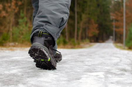 A man walks on a slippery road, the first snow in the park, winter shoes, the road is covered with slippery ice.の写真素材