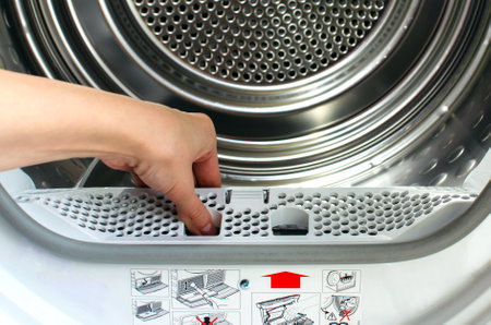 A housewife holds a lint trap from a front-loading tumble dryer. Womans handの写真素材