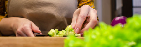 Close up view of the salad preparation process. A woman in an apron cuts a cucumber on a wooden...