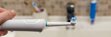 Hand with an electric toothbrush on a light background, charger