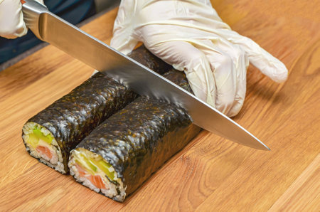 The process of making Japanese sushi. Knife in hand cuts a roll close-up on a wooden board.の写真素材