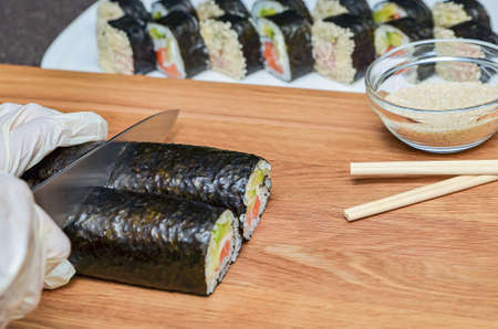 The process of making Japanese sushi. Knife in hand cuts a roll close-up on a wooden board.の写真素材