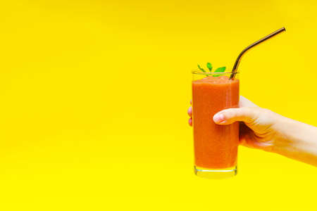 Childs hand holds a smoothie with strawberries and a metal cocktail tube in a glass glass, on a yellow background with copy spaceの写真素材