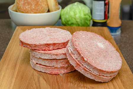 Frozen beef burger patties are placed on a wooden cutting board before cooking. Freezing in the freezer.の写真素材