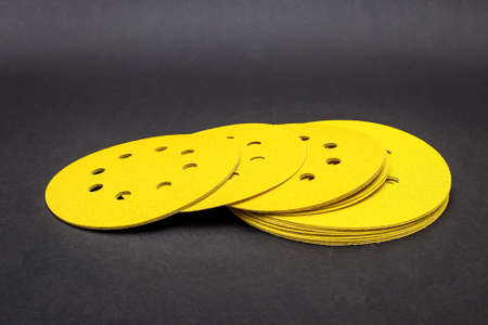 Sandpaper for sanding wood, on a black background. A stack of yellow round sandpaper. Copy space