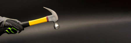 a workers hand in a glove holds a hammer on a black background. Postcard or poster on a work topic.の写真素材