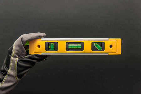 Hand in gloves holds a yellow building level on a black background. Postcard or poster for print, place for textの写真素材