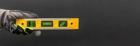 Hand in gloves holds a yellow building level on a black background. Postcard or poster for print, place for textの写真素材
