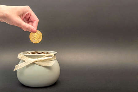 Investments, accumulation in cryptocurrency. Bitcoin in hand, female hand puts a gold bitcoin coin into a pot of coins. digital money, place for textの写真素材
