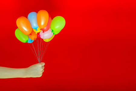 Gel balloons in a childs hand, on a red background, suitable for printing a postcard, poster or banner, place for text.の写真素材
