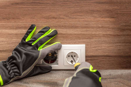 Installing electrical outlets. The electrician installs a decorative frame on the electrical outlets. Screwdriver in the hands of a master installing a socket with glovesの写真素材