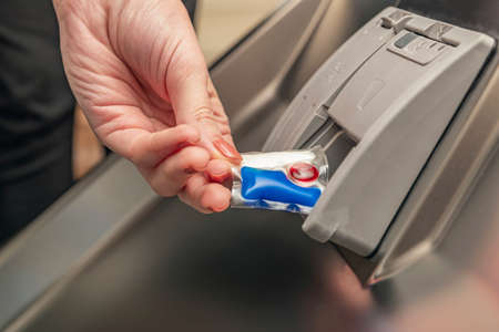 Dishwasher capsule, woman puts the capsule in the dishwasher before washing the pasta