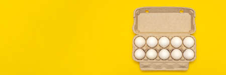 White eggs in a cardboard box on a yellow background. Top view, postcards for printing, advertising, place for text, large size.の写真素材