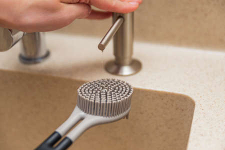 Liquid soap dispenser in the kitchen. A woman uses a liquid soap dispenser, a silicone brush for washing dishes.の写真素材