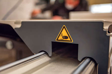 A warning sign on a woodworking machine. Production safety in a carpentry workshop. Hazard sign of...