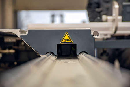 A warning sign on a woodworking machine. Production safety in a carpentry workshop. Hazard sign of moving parts in yellow triangle with handsの写真素材