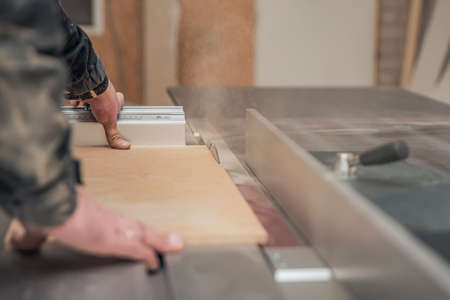 A carpenter works on a woodworking machine. Saws furniture pieces with a circular saw. The process...