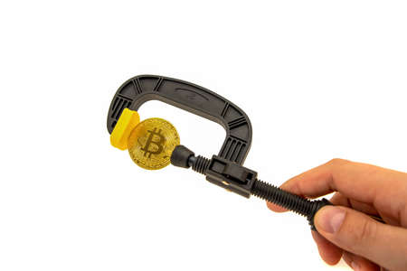 Pressure on bitcoin. Bitcoin is clamped in a vice on a white background. Prohibition of...