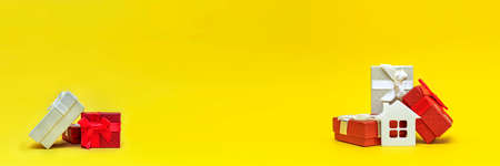 Real estate gift, home gift. White toy house in a gift box on a yellow background. Postcard for printing, banner with place for text.の写真素材