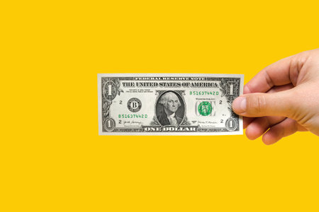 Money in hand, banknote in hand. Hand holding one dollar banknote isolated on yellow background. Banner with a yellow background on financial topics, place for text.の写真素材