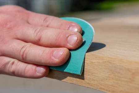 A carpenter is grinding a wooden board with sandpaper. The process of making wooden furniture. Hands of the master close-up.の写真素材