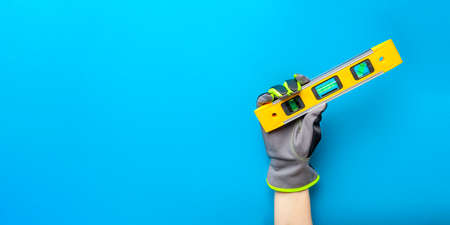 Building level. Hand in gloves holds a yellow building level on a blue background. Postcard or poster for print, place for textの写真素材