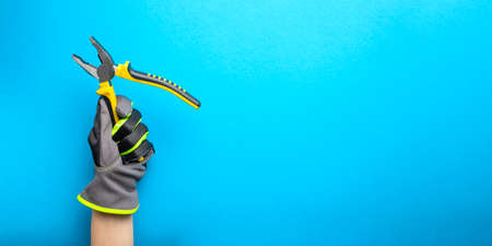 Pliers. Yellow and black pliers in the hand of an electrician on a blue monochrome background. Repair and installation tool. Banner for the design and printing of construction topics.の写真素材