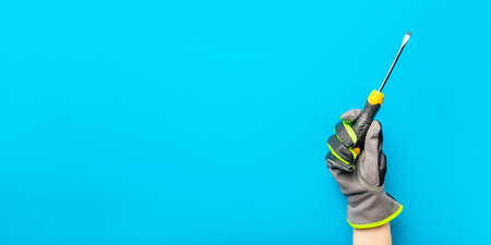 Screwdriver. Yellow and black screwdriver in the hand of an electrician on a blue monochrome background. Repair and installation tool. Banner for the design and printing of construction topics.の写真素材