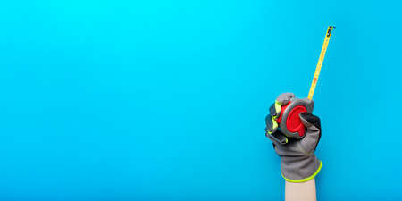 Tape measure. Holding a tape measure on a blue background. Repair and installation tool. Banner for...