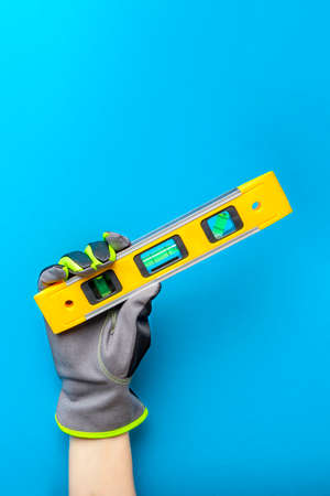 Building level. Hand in gloves holds a yellow building level on a blue background. Postcard or...