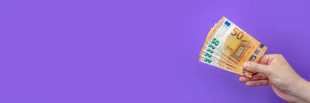 Money in hand, poster with banknote in hand. Hand holding 50 euro banknotes isolated on purple background. Banner with purple background on financial themesの写真素材