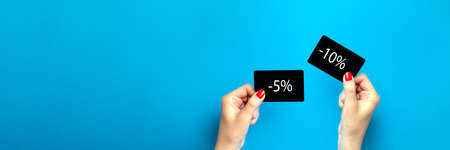 Discount card in hand. Discount on purchases 5 , 10 , percent . A woman is holding a black discount card on a blue background. Banner or poster for advertising or print. Place for textの写真素材
