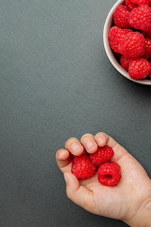 Raspberries in a saucer on a black background. The child takes raspberries from the plate. Shale...