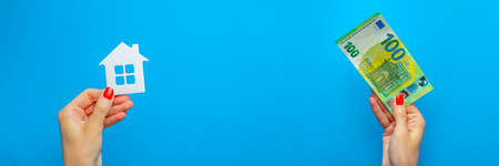 Sell a house, buy a house. House model in hand on a blue background. Payment for real estate. Banner on the theme of real estate.の写真素材