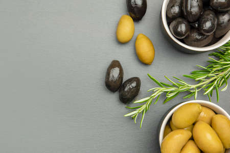 Black and green olives. Bella di cerignola Italian olives. Colored olives and a sprig of rosemary lie on a black stone countertop. Culinary banner or poster for advertising with place for textの写真素材