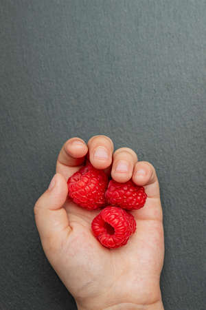 Raspberries in a saucer on a black background. The child takes raspberries from the plate. Shale...