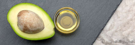 Avocado oil. An avocado with a bone lies on a stone tray. Avocodo oil is poured into a plate. Banner...