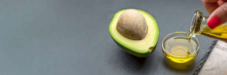 Avocado oil. An avocado with a bone lies on a stone tray. Avocodo oil is poured into a plate. Banner...