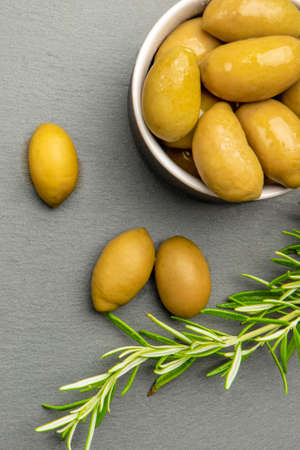 Green olives. Bella di cerignola Italian olives. Colored olives and a sprig of rosemary lie on a black stone countertop. Culinary banner or poster for advertising with place for textの写真素材