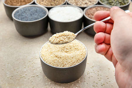 White sesame seeds, sesame seeds in a black saucer on a background of various seeds. Male hand sprinkles sesame seeds with a spoonの写真素材