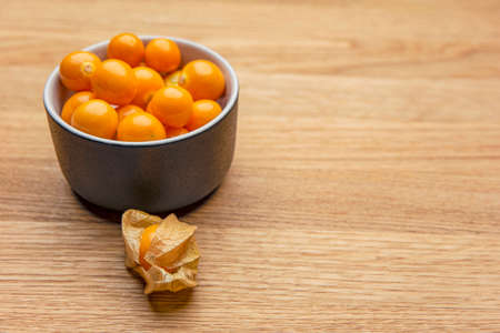 Physalis fruits on a wooden table. Sweet yellow physalis berries in a cup on wood backgroundの写真素材