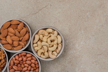 Peanuts and almonds in cups on a marble table top, top view. Superfoods and healthy eating concept