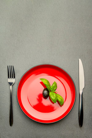 Diet. Small amount of food on the plate. One olive is in a red plate, a knife and a fork. Weight loss and diet concept. Empty space for textの写真素材